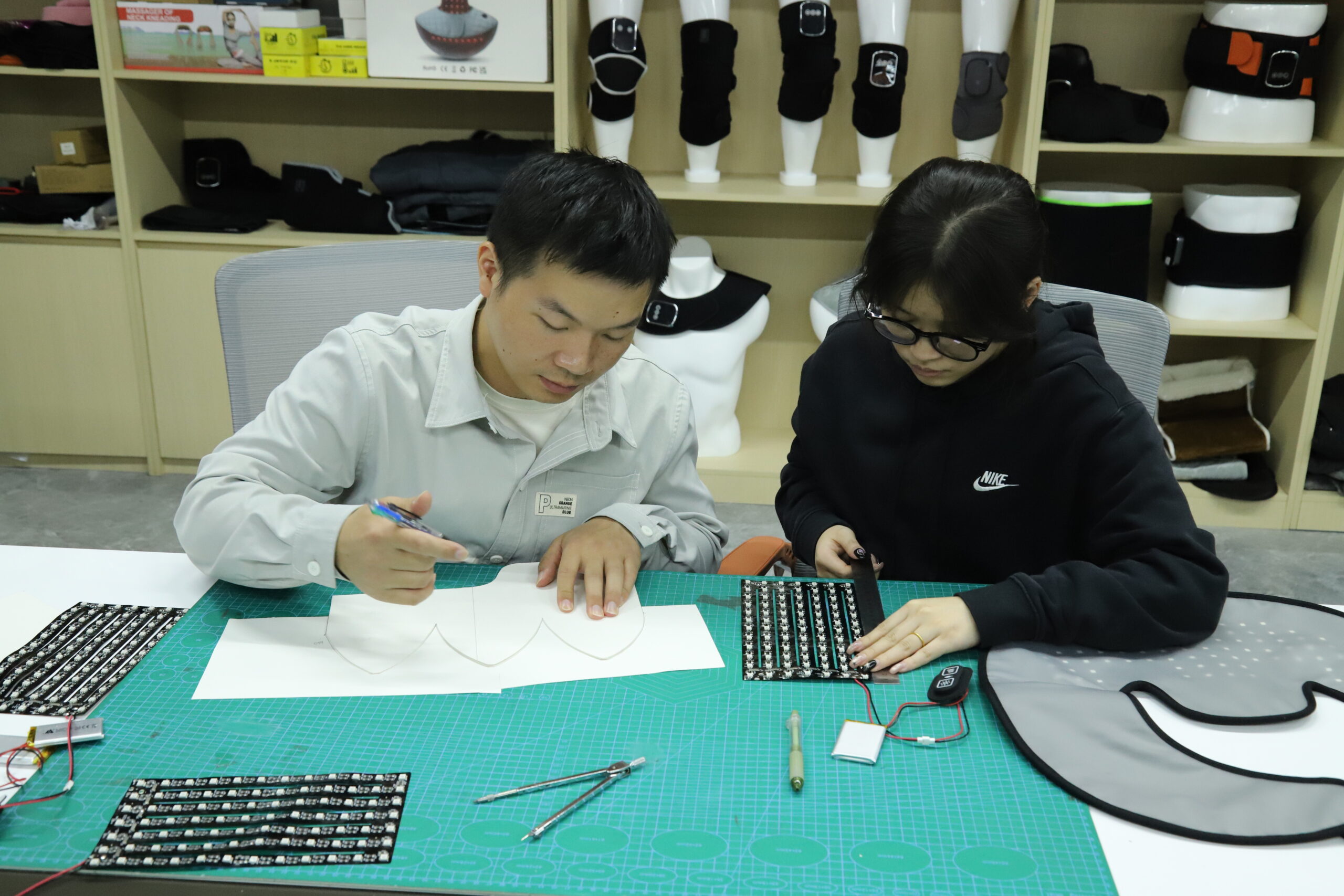Dos personas revisando un componente de producto y un dibujo en una mesa de trabajo de la fábrica.
