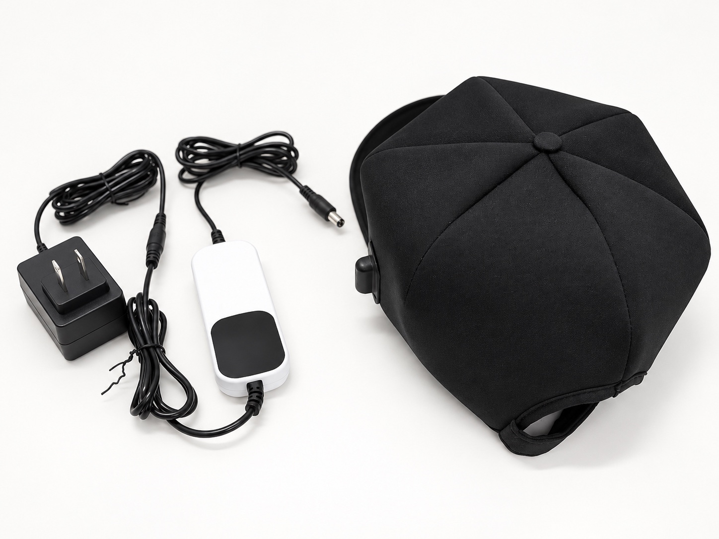 Gorra negra con cable, mando, adaptador de corriente y cables sobre un fondo neutro.